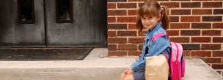 Photo: Little girl sitting outside school with her backpack and snacks