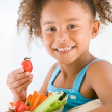 Photo: Girl Smiling and Holding a Tomato